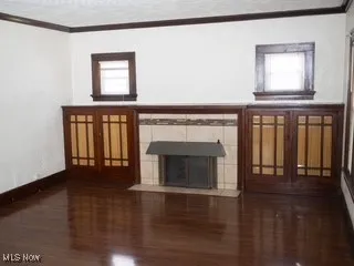 Unfurnished living room with wood finished floors, ornamental molding, and a tile fireplace