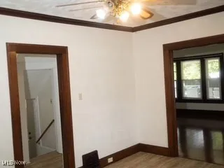Empty room with a ceiling fan, crown molding, and wood finished floors