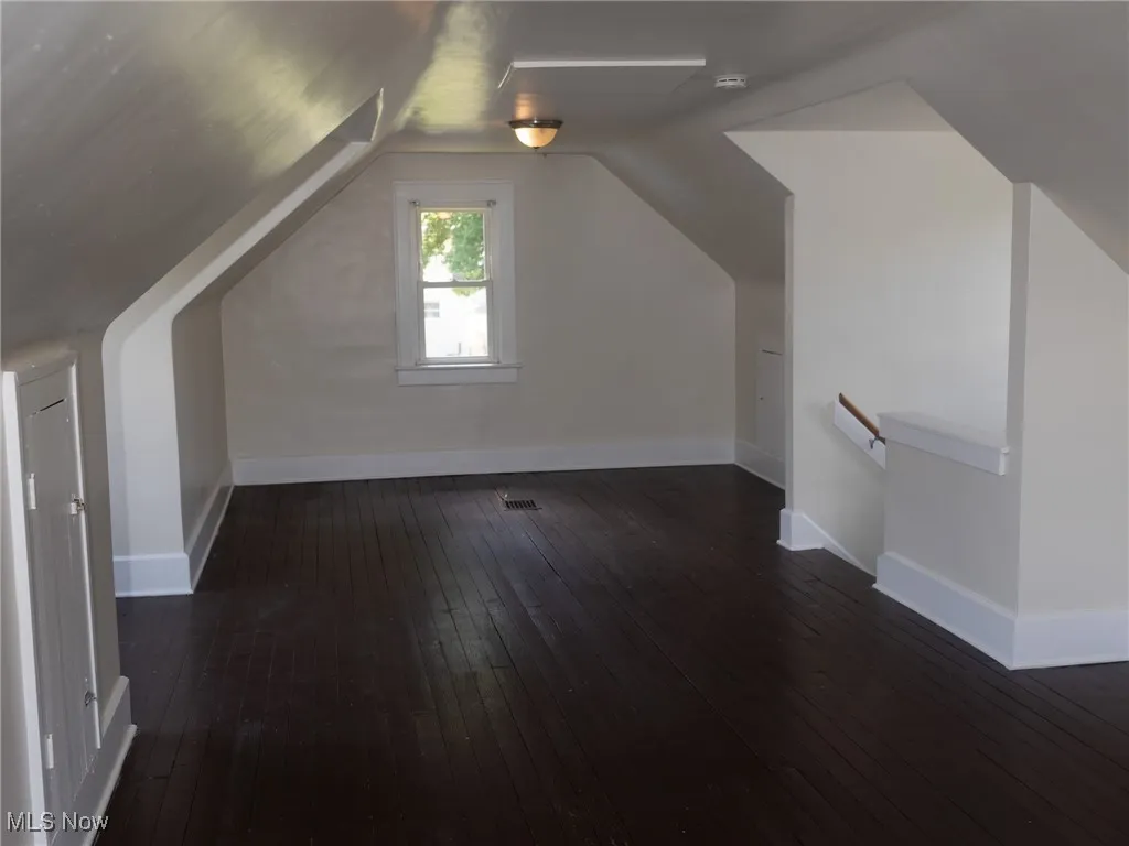 Additional living space featuring dark wood-style flooring and vaulted ceiling