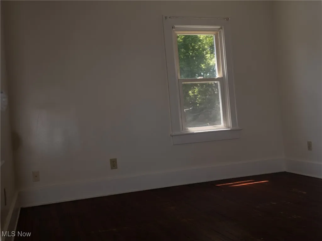Empty room featuring dark wood-style flooring and baseboards
