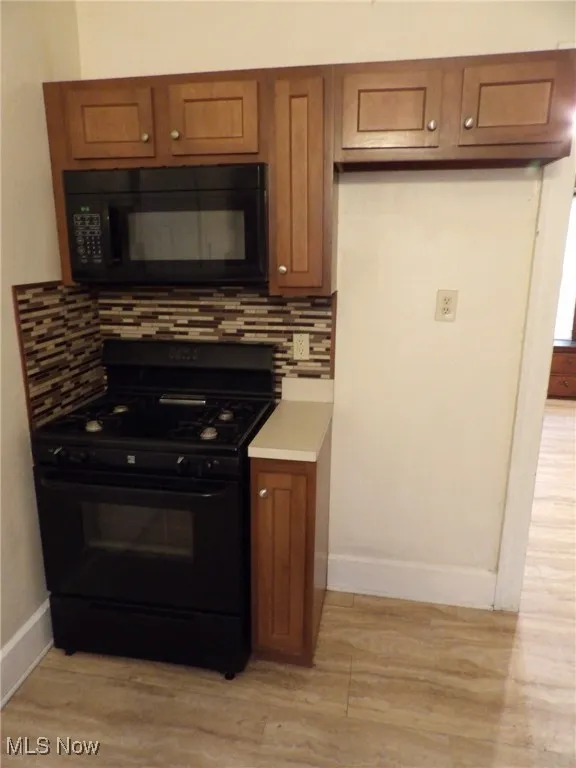 Kitchen featuring black appliances, brown cabinetry, backsplash, baseboards, and light wood-type flooring