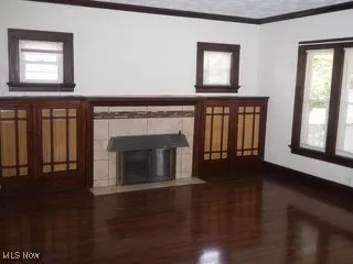 Unfurnished living room with ornamental molding, wood finished floors, and a tiled fireplace