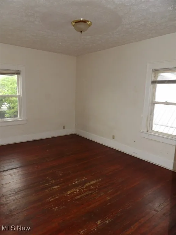 Spare room featuring dark wood finished floors, baseboards, and a textured ceiling