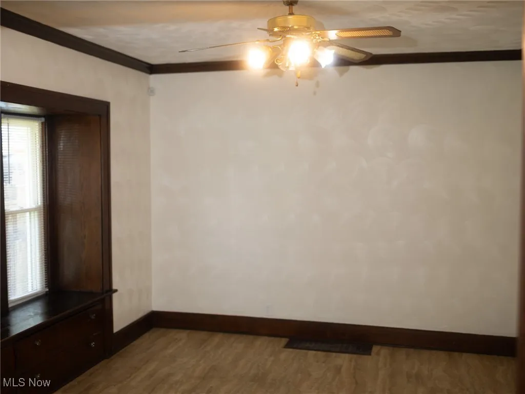 Unfurnished room featuring crown molding, dark wood-style flooring, and ceiling fan