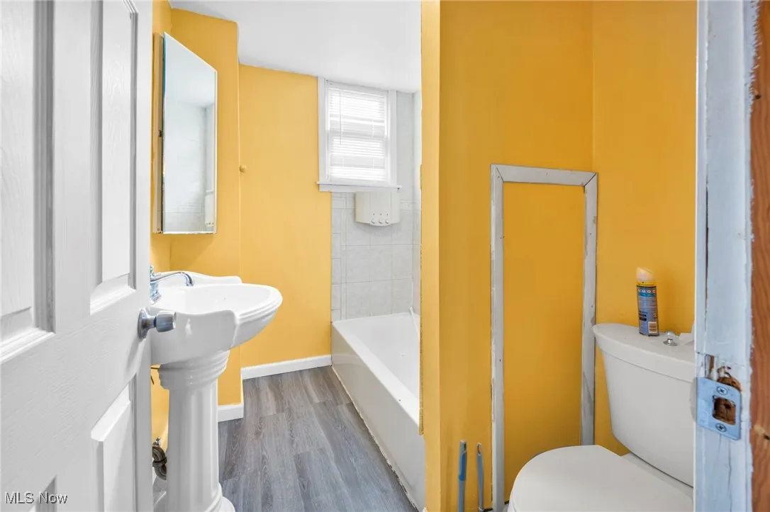 Full bathroom with a bathtub, toilet, wood finished floors, and baseboards