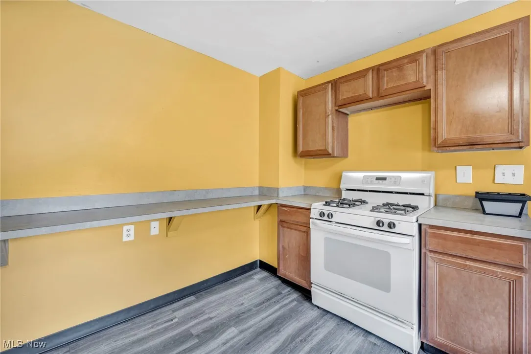 Kitchen featuring white gas range, wood finished floors, light countertops, and brown cabinets