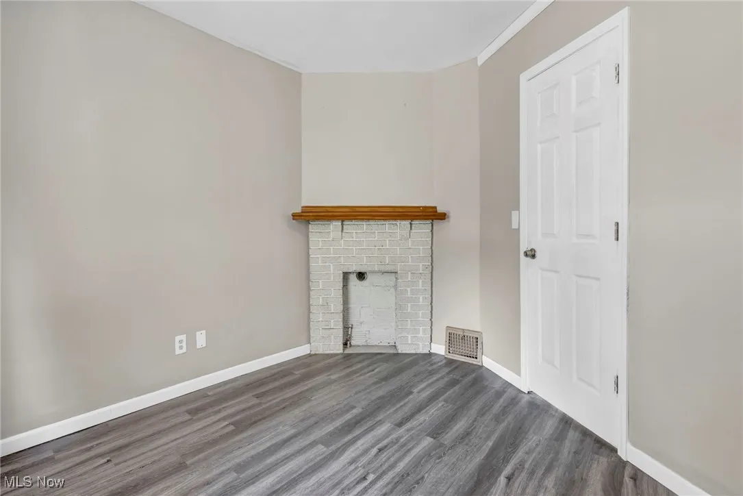 Unfurnished living room featuring wood finished floors, baseboards, crown molding, and a fireplace