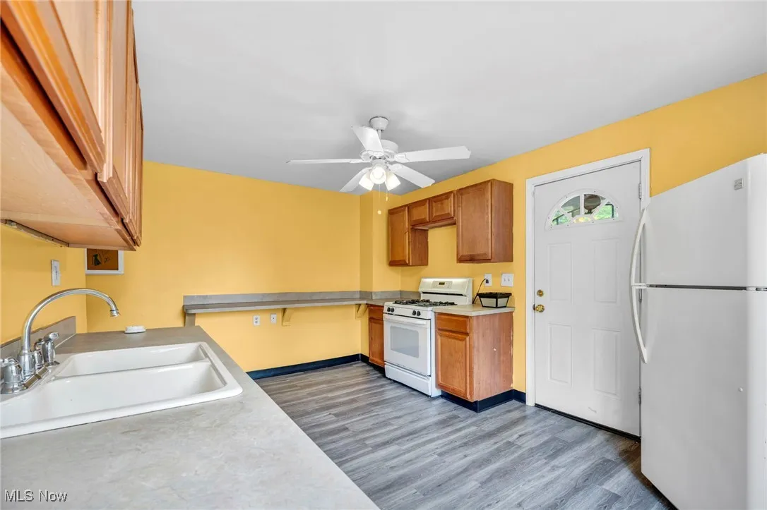 Kitchen with white appliances, a sink, light countertops, light wood finished floors, and a ceiling fan