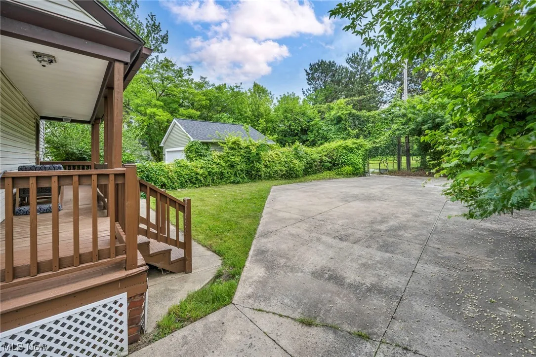 View of green lawn featuring a wooden deck, a patio area, and view of scattered trees