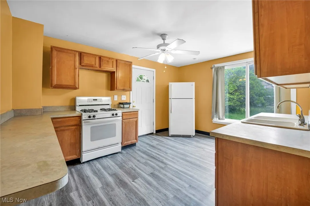 Kitchen with white appliances, a sink, light countertops, and ceiling fan