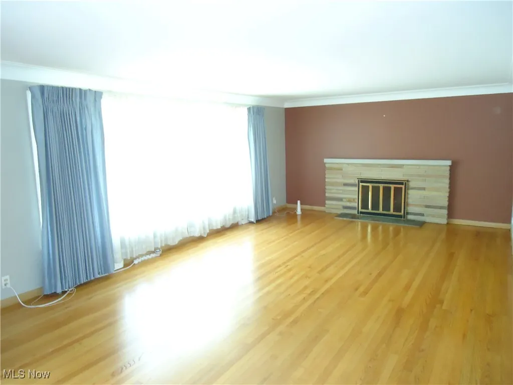 Unfurnished living room featuring crown molding, light wood-style flooring, and a glass covered fireplace