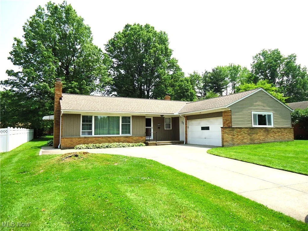 Ranch-style house featuring a chimney, an attached garage, driveway, and brick siding