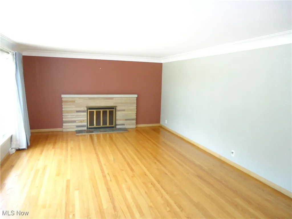 Unfurnished living room featuring crown molding, a glass covered fireplace, light wood-style flooring, and baseboards