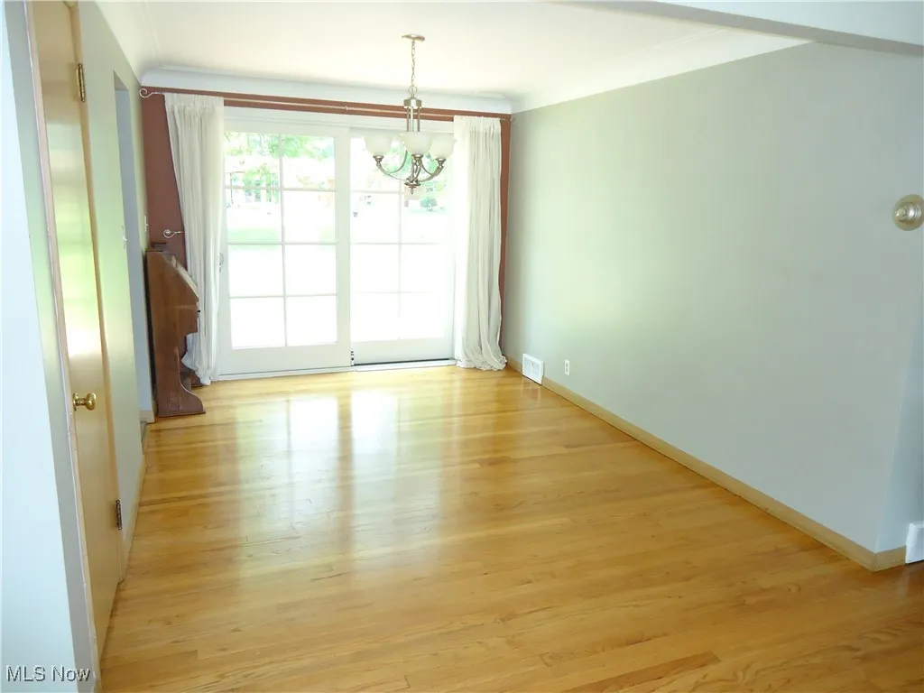 Spare room featuring a chandelier, light wood-style flooring, ornamental molding, and baseboards