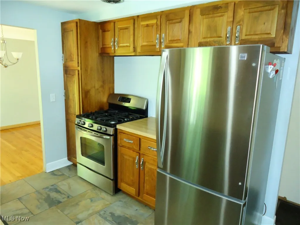 Kitchen with appliances with stainless steel finishes, brown cabinets, light countertops, and a chandelier