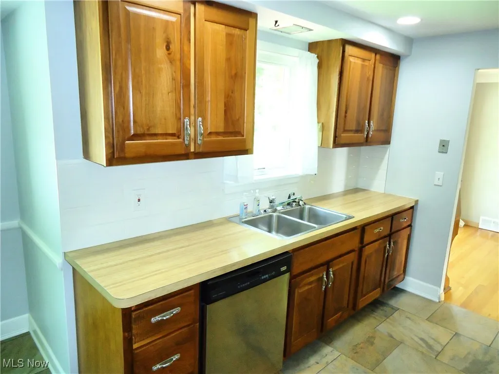 Kitchen featuring dishwasher, a sink, baseboards, brown cabinets, and backsplash