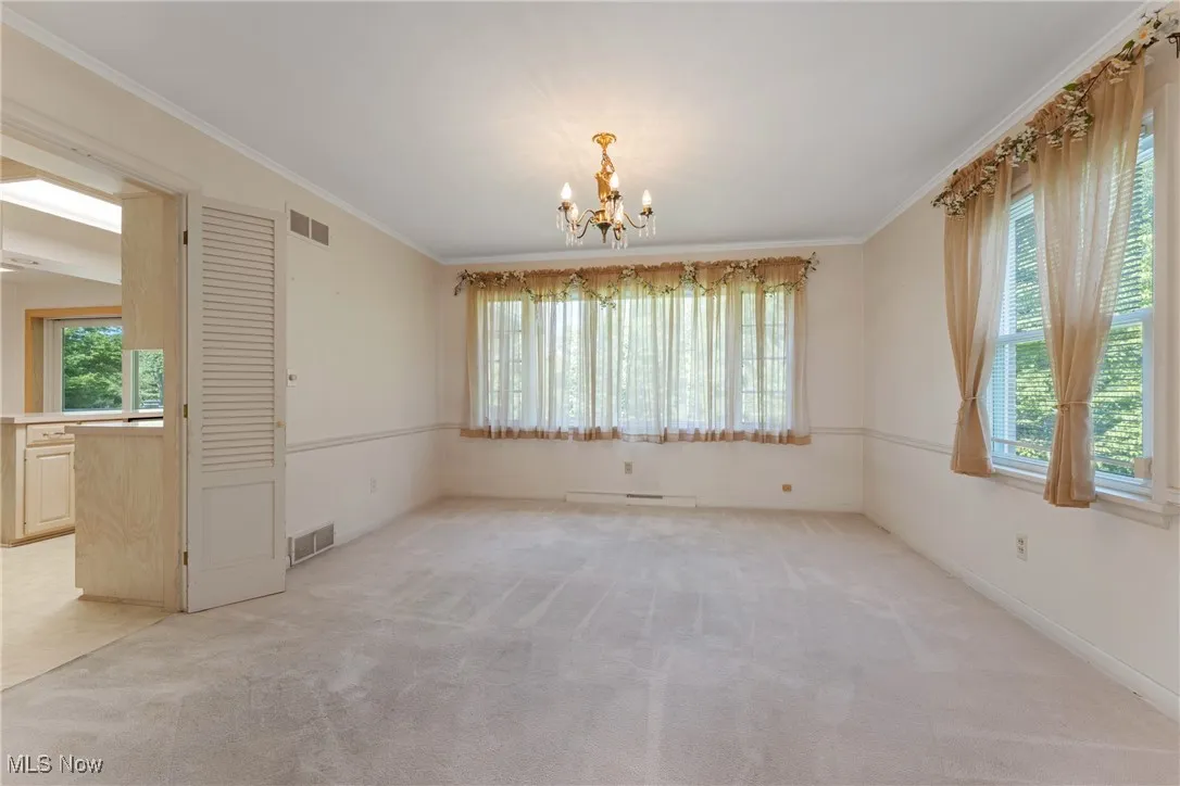 Unfurnished room featuring a chandelier, plenty of natural light, light colored carpet, and crown molding