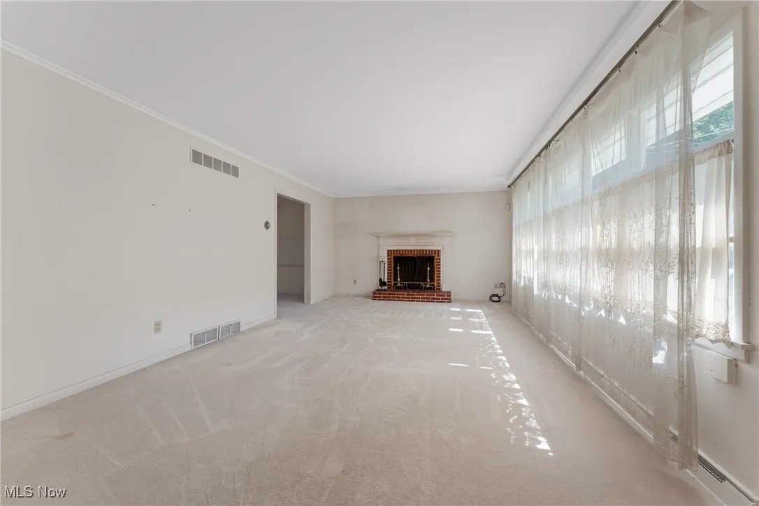 Unfurnished living room featuring light colored carpet, a brick fireplace, and crown molding