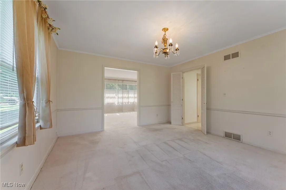 Unfurnished room with a chandelier, ornamental molding, and light colored carpet