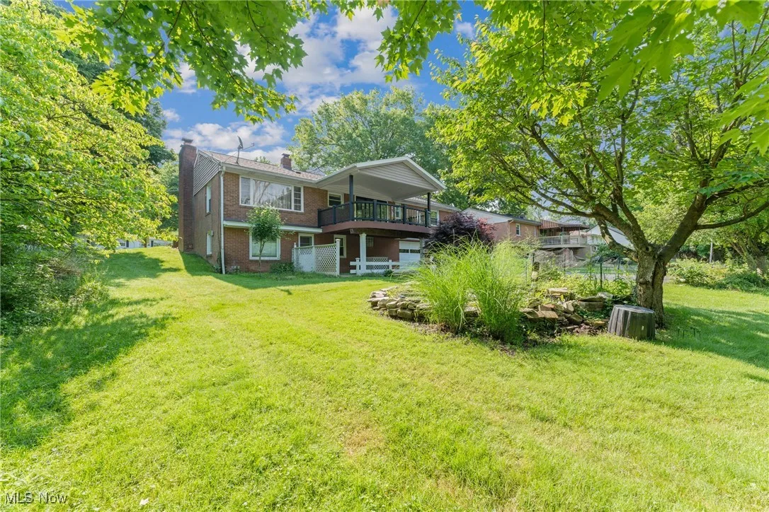 Back of property with brick siding, a chimney, a lawn, and a wooden deck