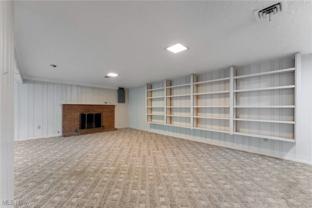 Unfurnished living room with carpet, a brick fireplace, and electric panel