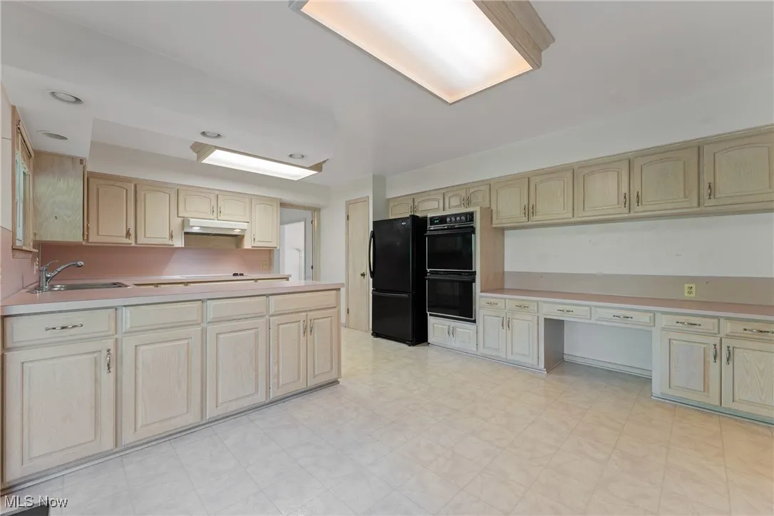 Kitchen featuring black appliances, under cabinet range hood, light countertops, light brown cabinetry, and light flooring