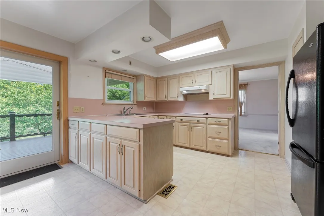 Kitchen featuring freestanding refrigerator, light brown cabinets, under cabinet range hood, light countertops, and a peninsula