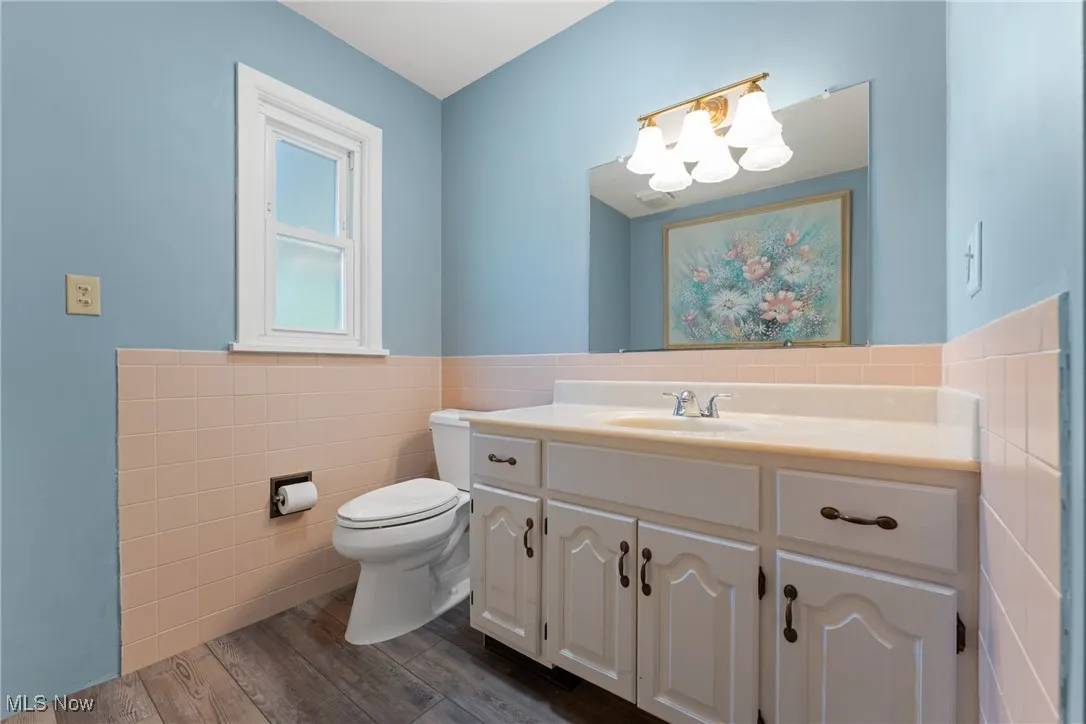 Half bath featuring tile walls, a chandelier, vanity, wood finished floors, and wainscoting