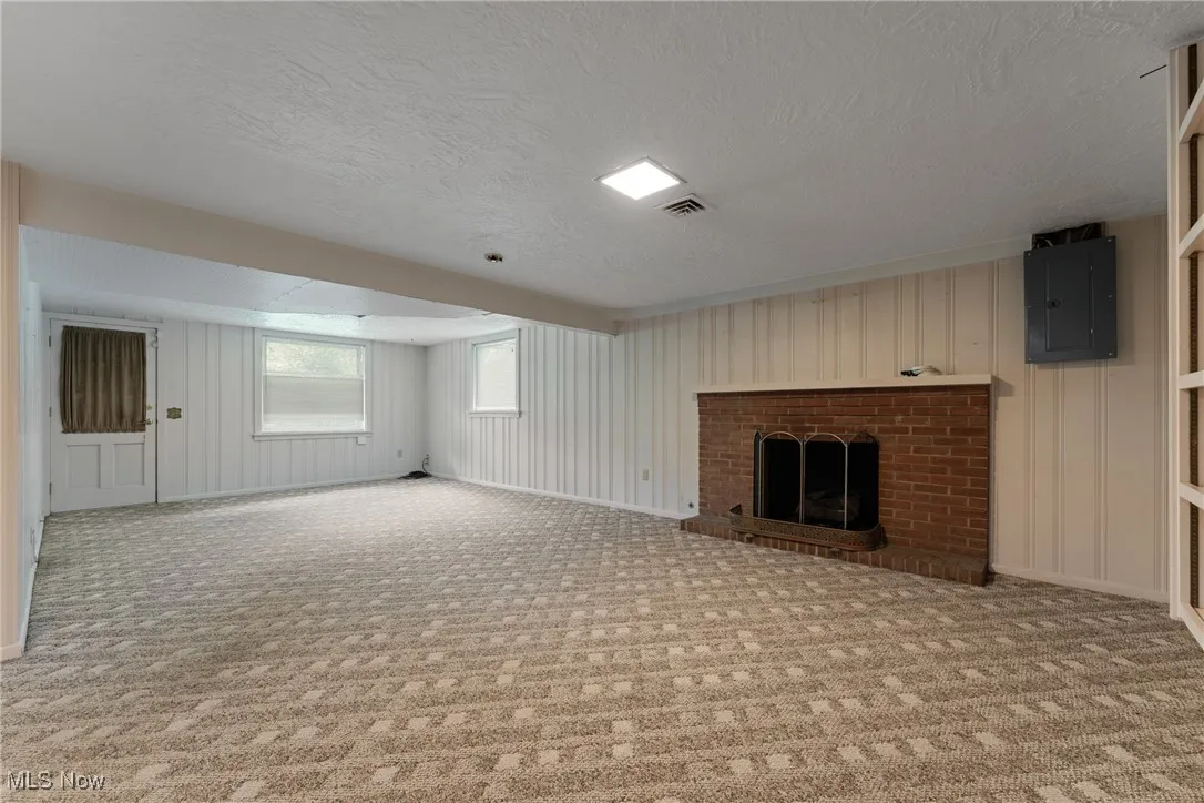 Unfurnished living room with electric panel, carpet flooring, a textured ceiling, and a fireplace