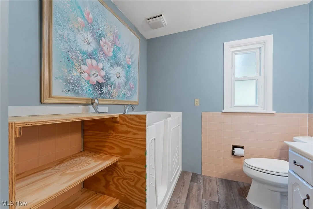 Bathroom featuring wood finished floors, tile walls, vanity, and wainscoting