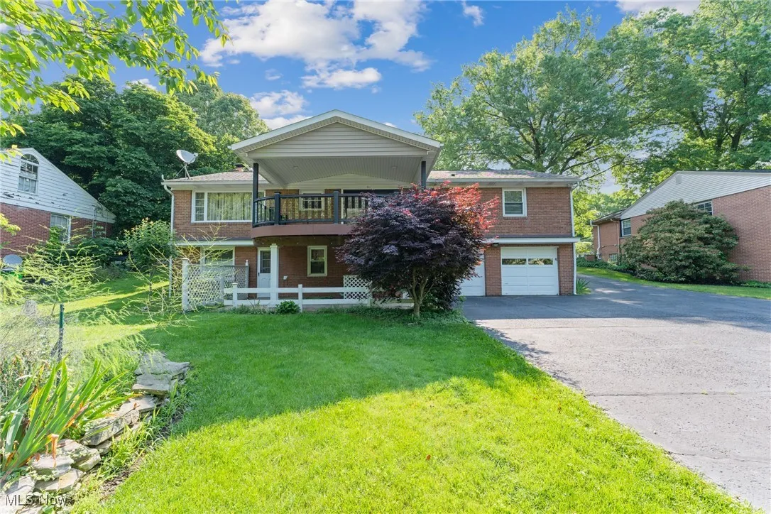 View of front facade with brick siding, asphalt driveway, a front yard, a garage, and a balcony