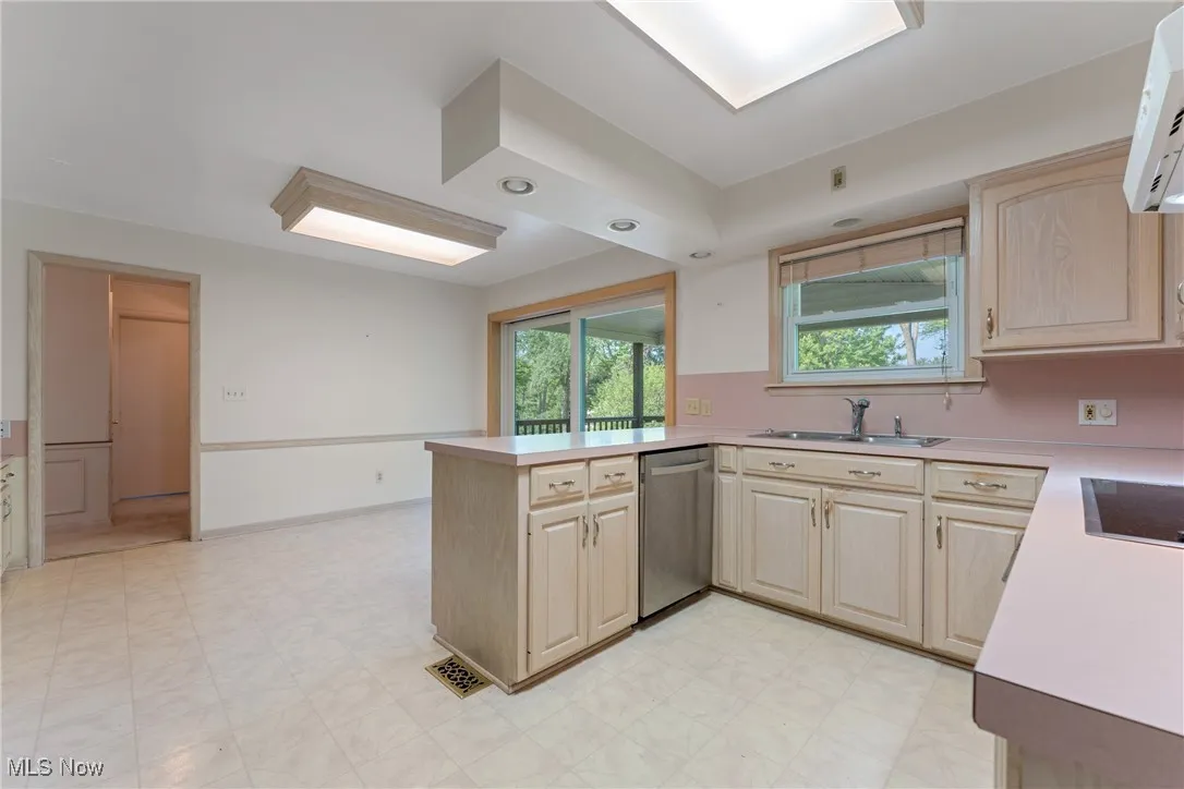 Kitchen with stainless steel dishwasher, a peninsula, light countertops, light brown cabinetry, and light floors