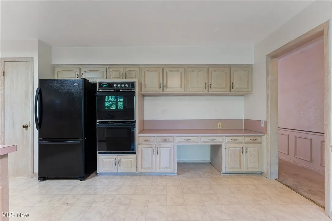 Kitchen with black appliances, light countertops, built in desk, and cream cabinets