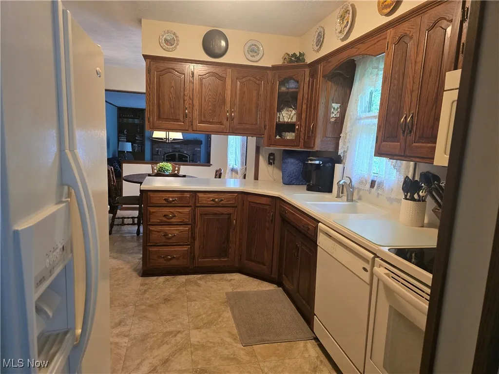 Kitchen featuring white appliances, light countertops, a sink, glass insert cabinets, and a peninsula