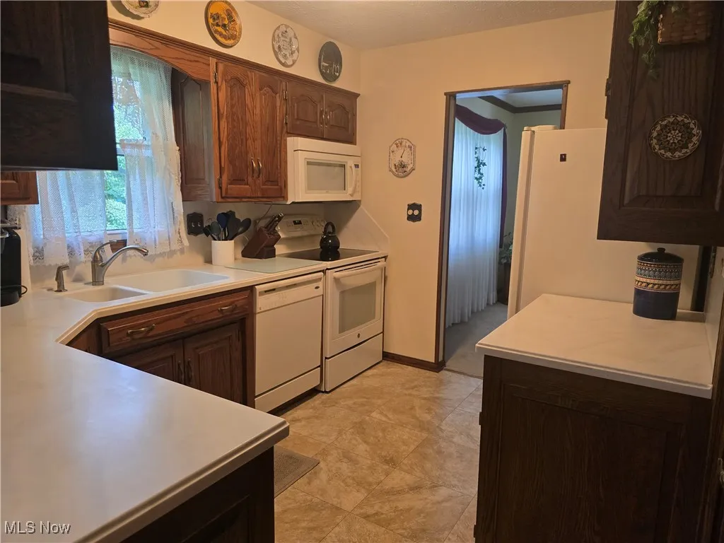 Kitchen featuring white appliances, a sink, Corian countertops, and dark brown cabinetry