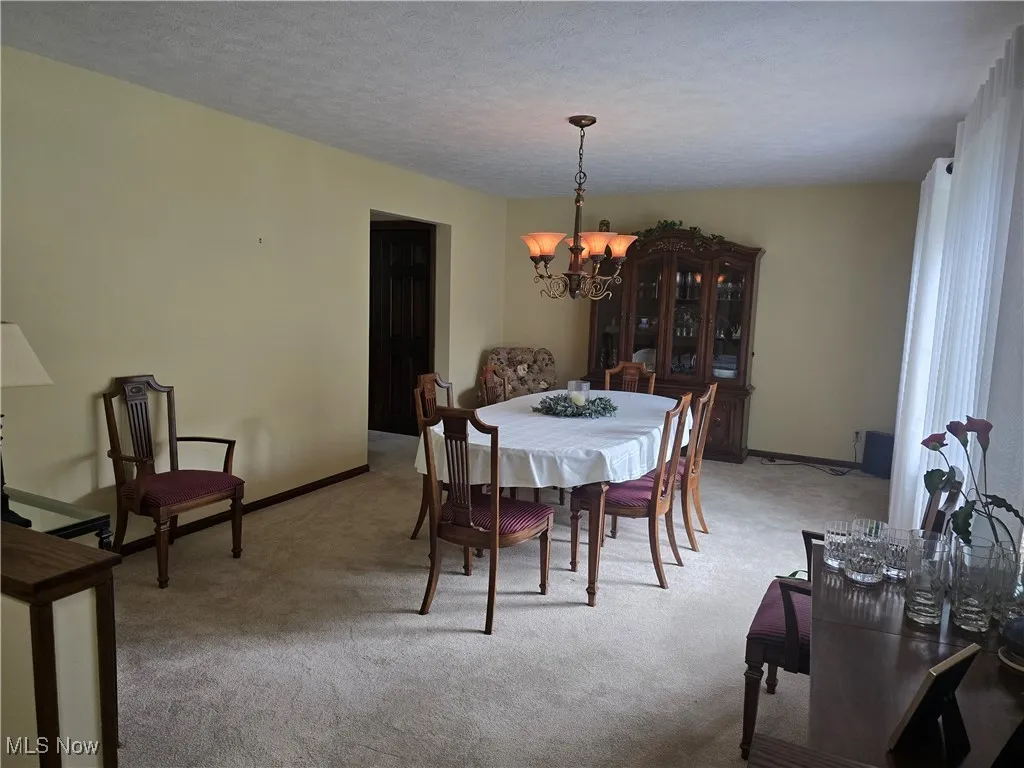 Dining space featuring a chandelier, light carpet, baseboards, and a textured ceiling