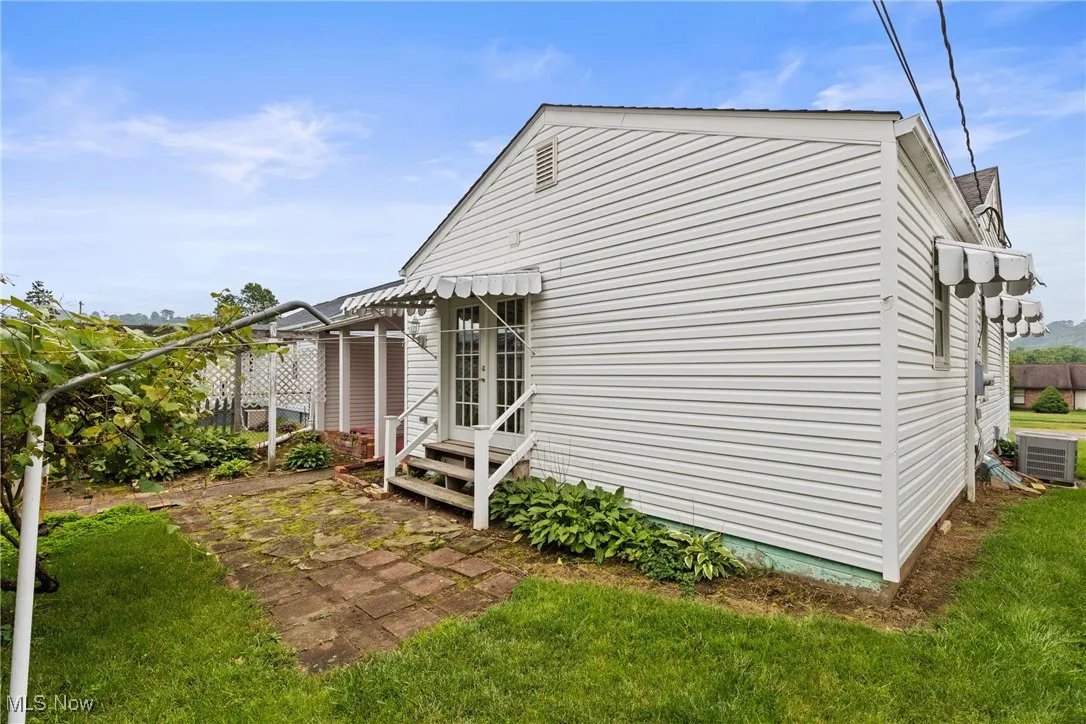 View of side of home with entry steps, central AC unit, and a yard