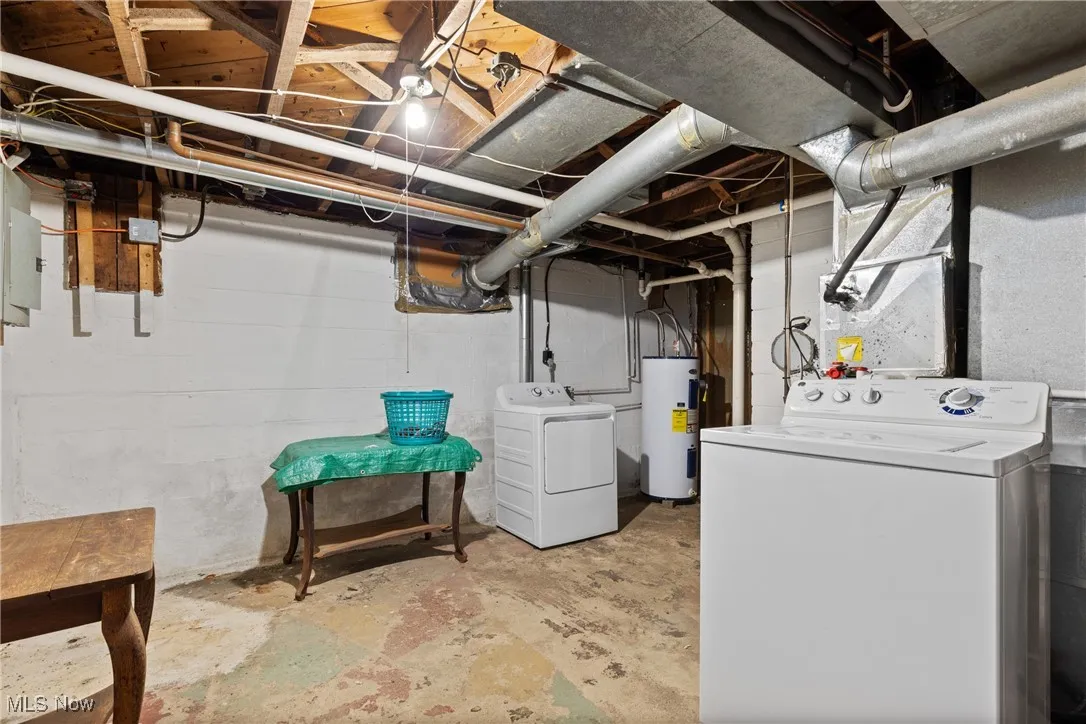 Unfinished below grade area featuring electric water heater and washer and clothes dryer