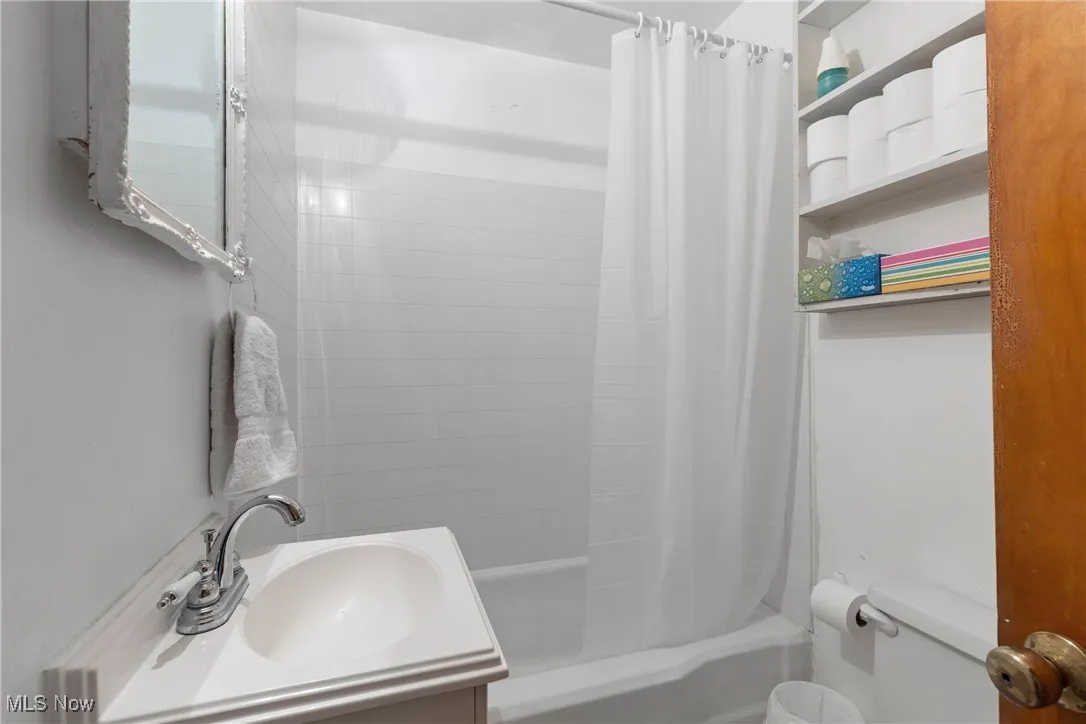Bathroom with toilet, shower / bath combination with curtain, and vanity