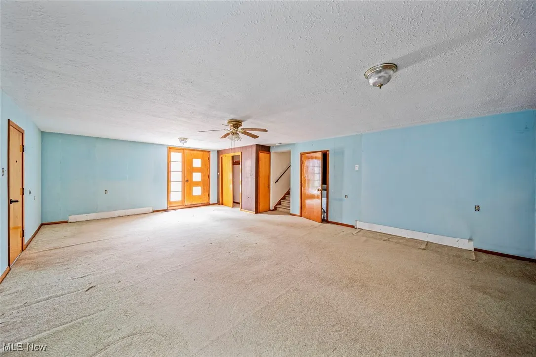 Spare room featuring a textured ceiling, baseboards, a ceiling fan, stairway, and carpet flooring