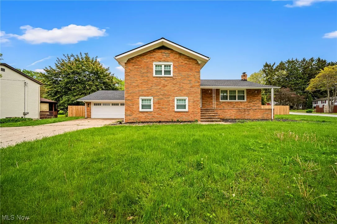 View of front facade with brick siding, a chimney, a front yard, a garage, and concrete driveway