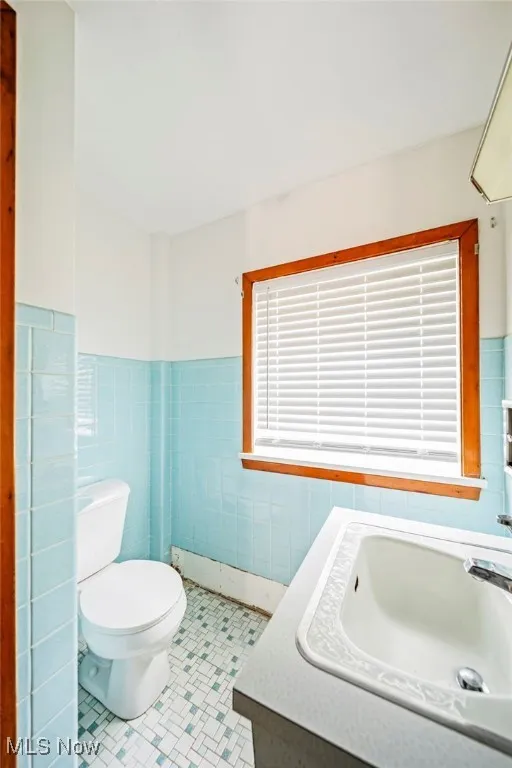 Bathroom with tile walls, toilet, tile patterned floors, a sink, and wainscoting