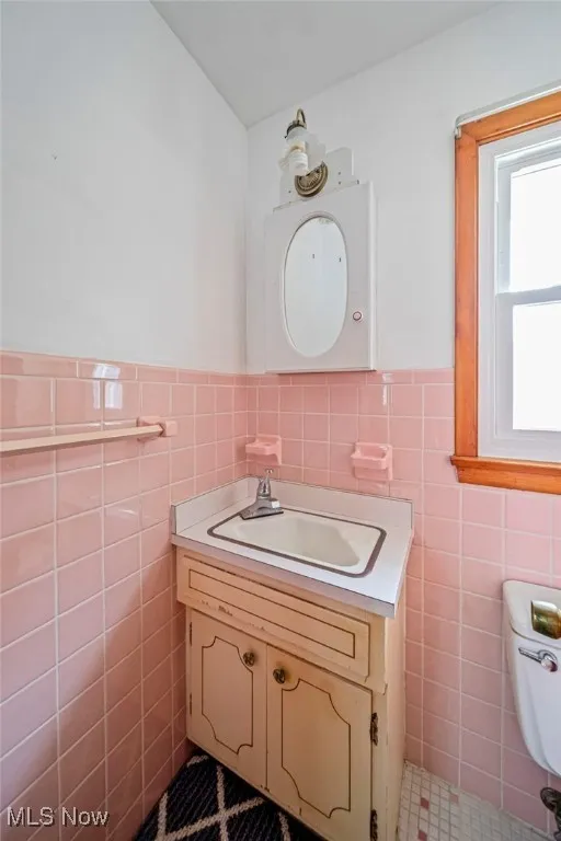 Half bathroom featuring tile walls, vanity, a wainscoted wall, and toilet