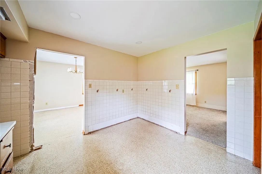 Spare room with a chandelier, tile walls, and speckled floor