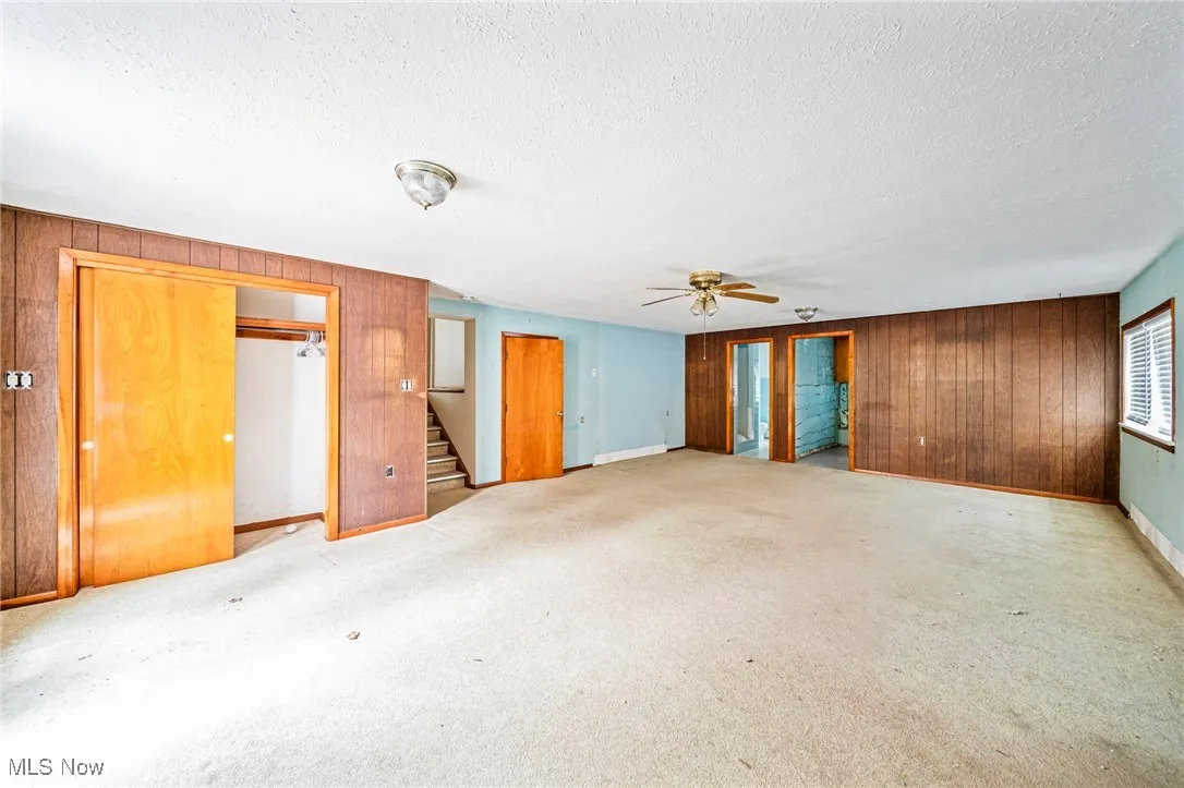 Unfurnished room with wood walls, stairway, a textured ceiling, a ceiling fan, and baseboards