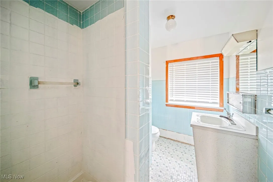Bathroom featuring tile walls, a sink, toilet, a tile shower, and tile patterned floors