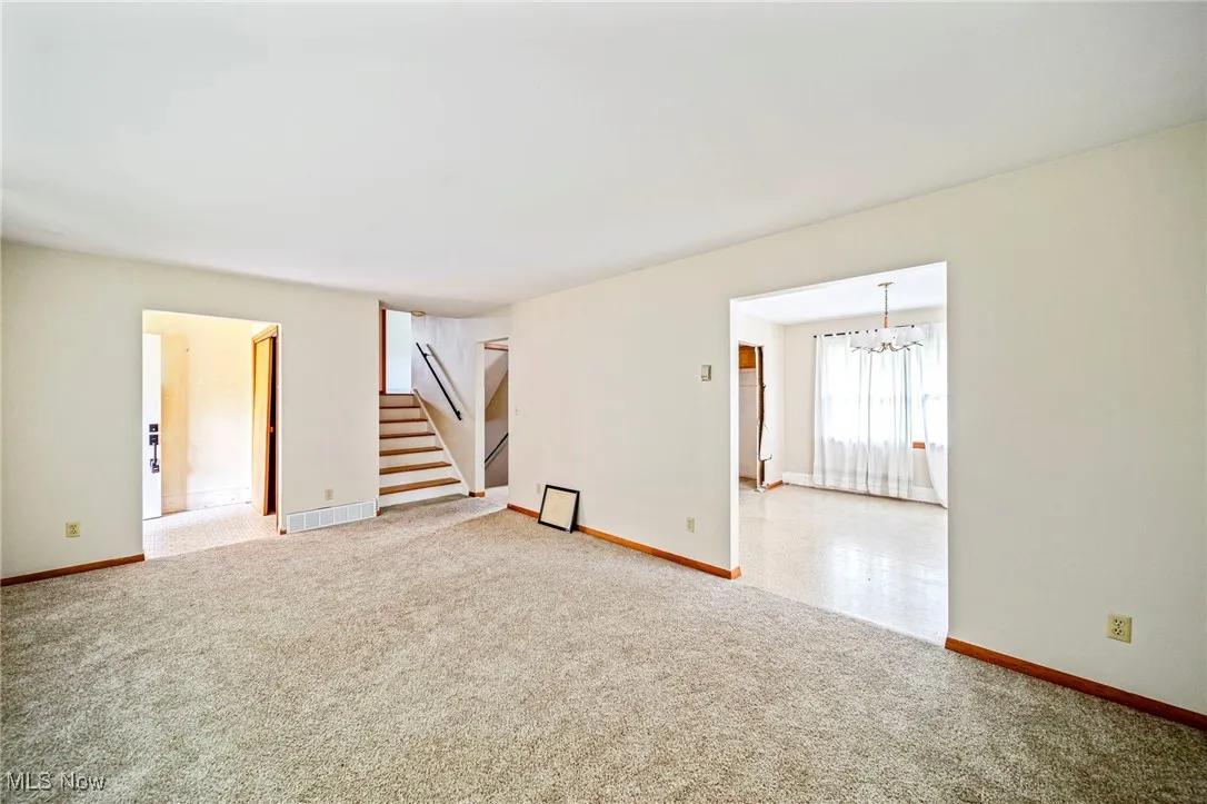 Spare room featuring stairs, a chandelier, light colored carpet, and baseboards