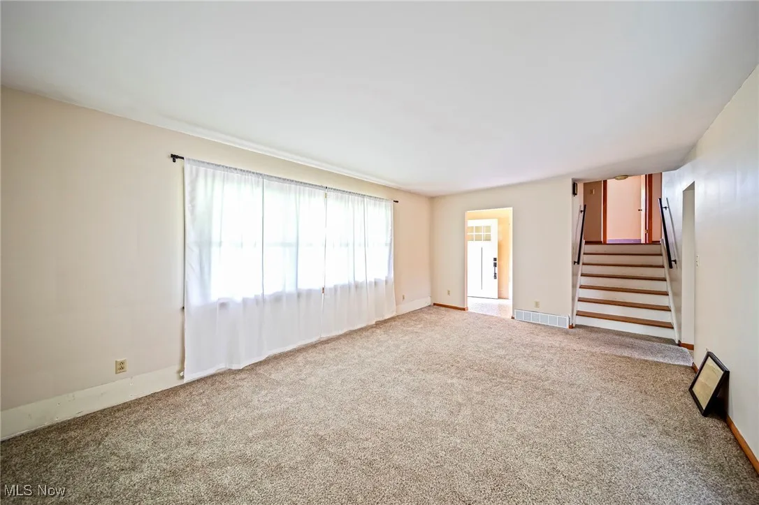Unfurnished living room featuring carpet flooring, stairway, and baseboards