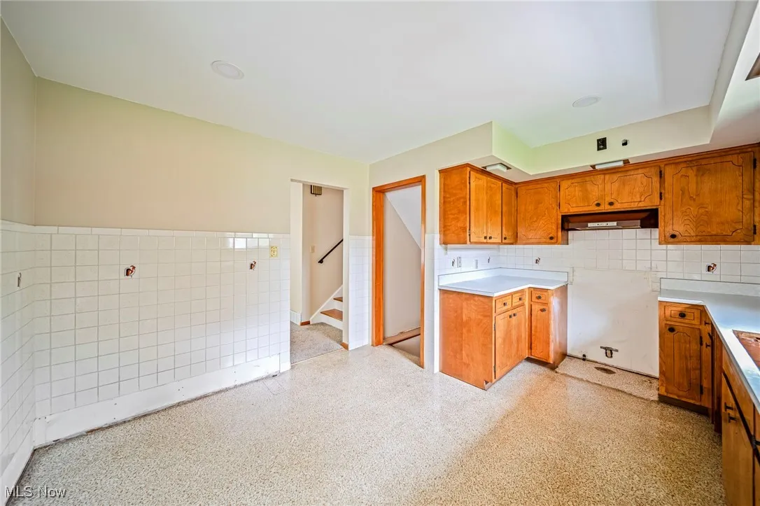 Kitchen with under cabinet range hood, tile walls, brown cabinets, a wainscoted wall, and light countertops