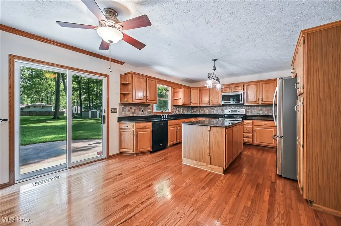 Kitchen with stainless steel appliances, granite countertops, a sink, a kitchen island, and open shelves